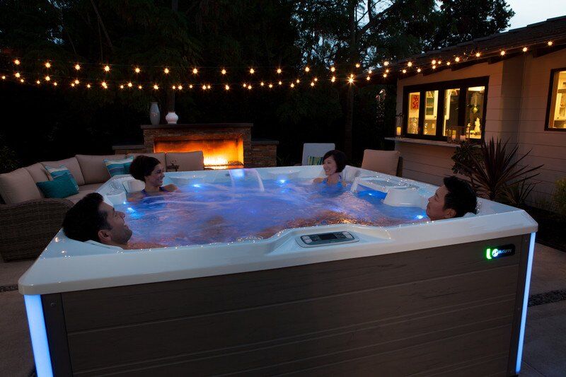 A group of friends relaxes in a Limelight Pulse hot tub after the summer sun goes down